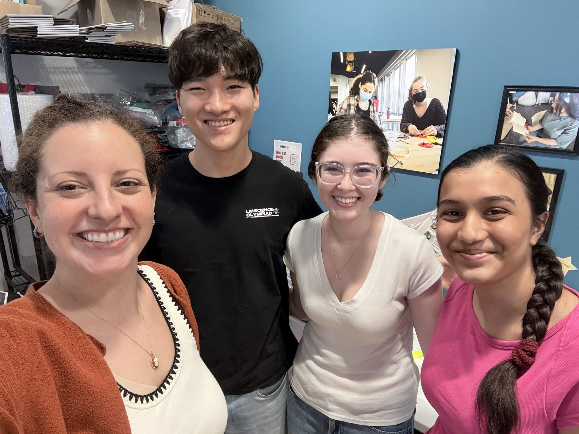 Three Adapt Project members and a staff member standing together and smiling at TechOWL, in a room lined with shelves of assistive devices and printing supplies.