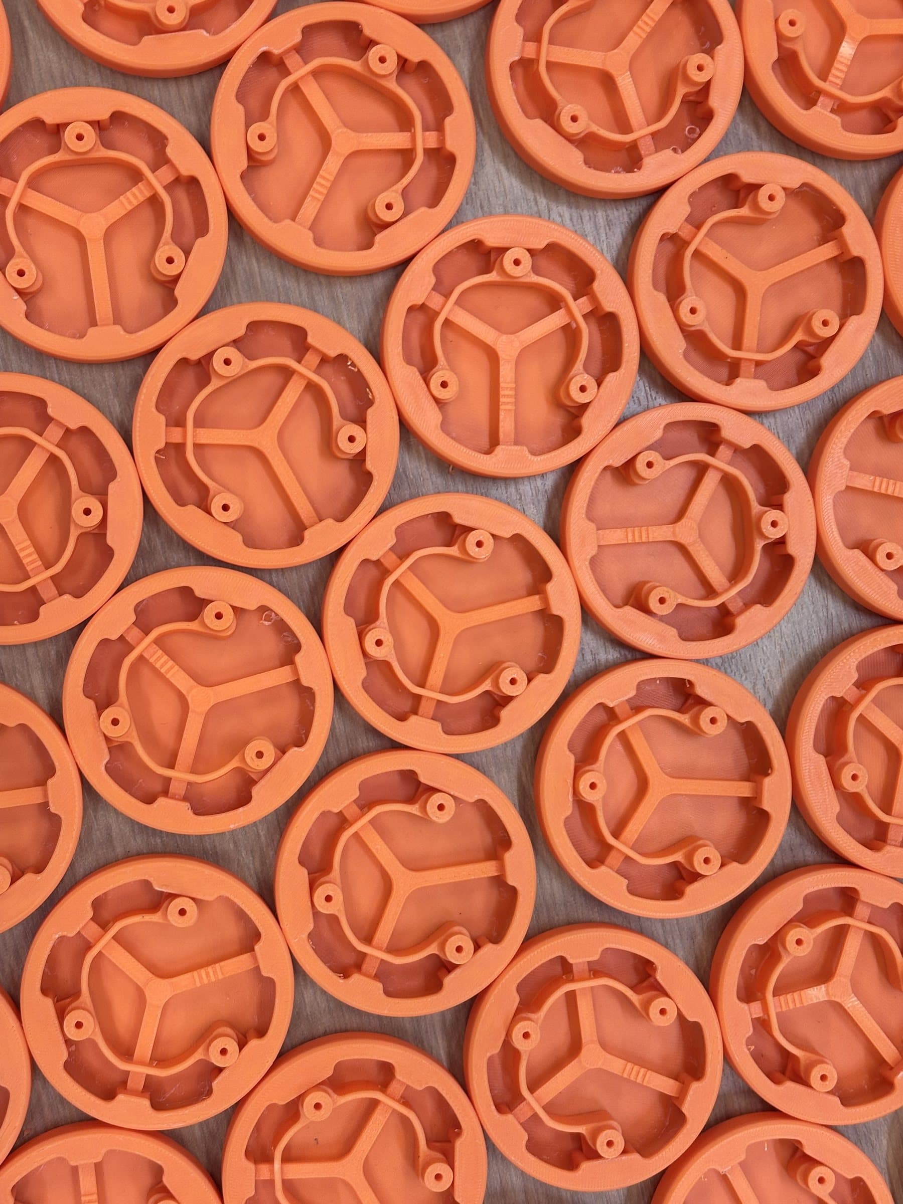 Dozens of orange 3D-printed switch button frames arranged edge to edge on a wood table.