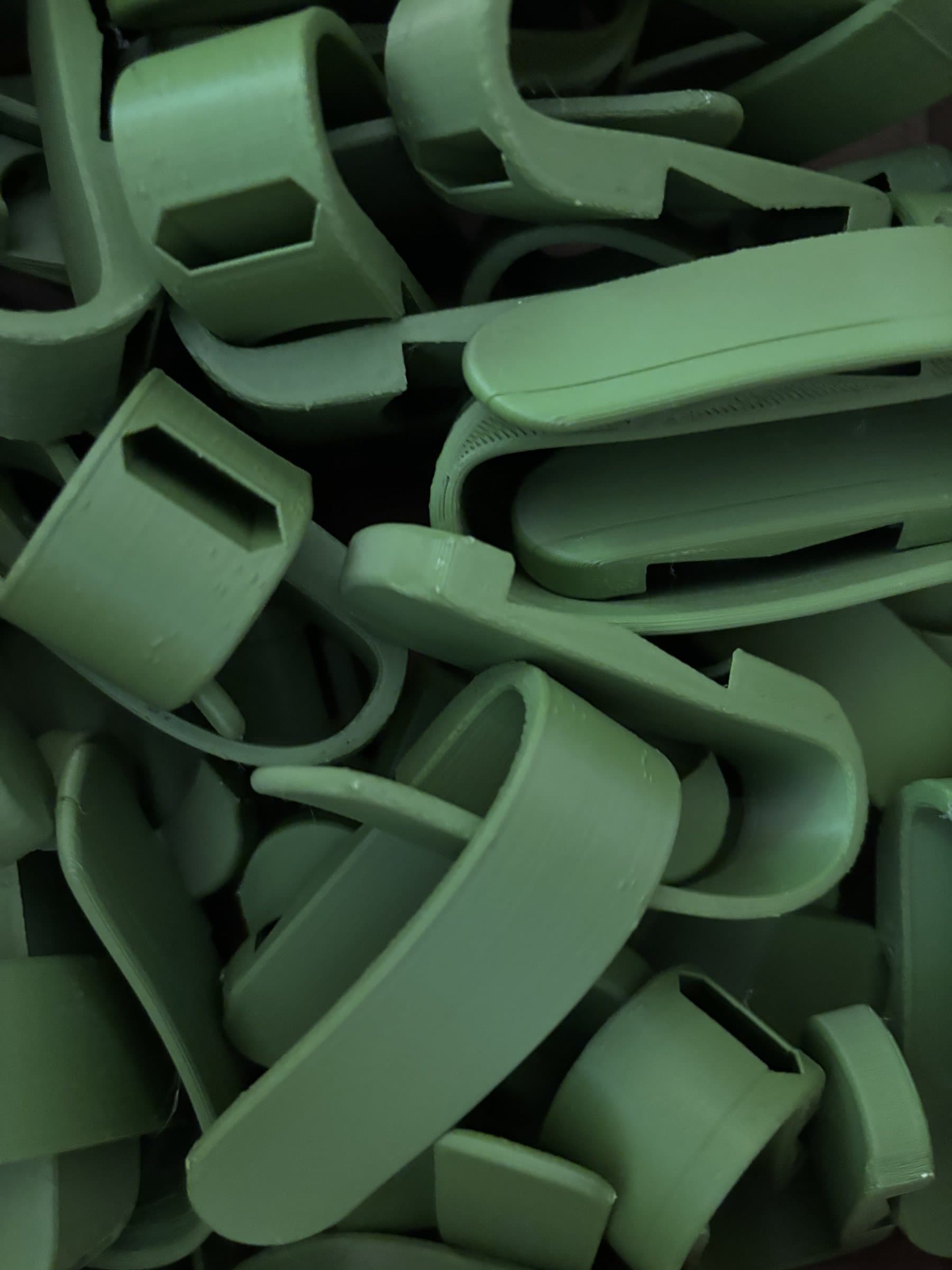 A bin filled with green 3D-printed universal cuffs, which hold forks, spoons, and other utensils for people with limited grip.